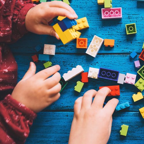 Children play and build with colorful toy bricks or plastic blocks on table. School or preschool background. Concept of kids leisure and education at home or class, early learning and development.